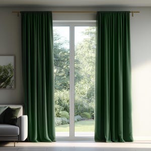 May include: A pair of floor-length, solid dark green curtains hanging from a simple gold-toned metal rod. The curtains feature vertical pleats and are positioned on either side of a large glass door that looks out onto a bright outdoor garden.