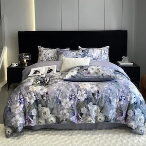 Könnte beinhalten: Ein Bett mit einer grauen und weißen Bettwäsche mit Blumenmuster und passenden Kissenbezügen. Das Bett hat ein schwarzes Kopfteil und einen weißen Teppich auf dem Boden.