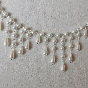 Op de afbeelding: Een witte parelketting met een cascade-ontwerp. De ketting heeft kleine ronde parels en grotere traanvormige parels.