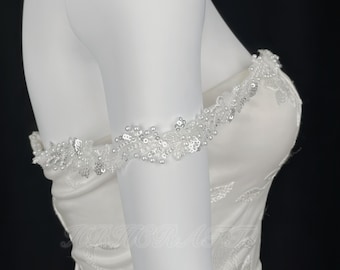 Puede incluir: Un vestido de novia blanco de hombros descubiertos con un ribete de encaje con cuentas alrededor del escote. El vestido está hecho de tejido de satén y tiene un corpiño ajustado.