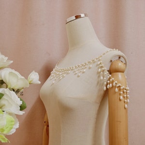 Op de afbeelding: Een witte parelketting met een delicate ketting en hangende parels. De ketting wordt getoond op een wit mannequin.