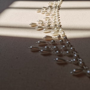 Op de afbeelding: Een lange streng witte parels met zilveren kettingaccenten. De parels zijn in een cascade-patroon gerangschikt, wat een delicate en elegante uitstraling cre&euml;ert.
