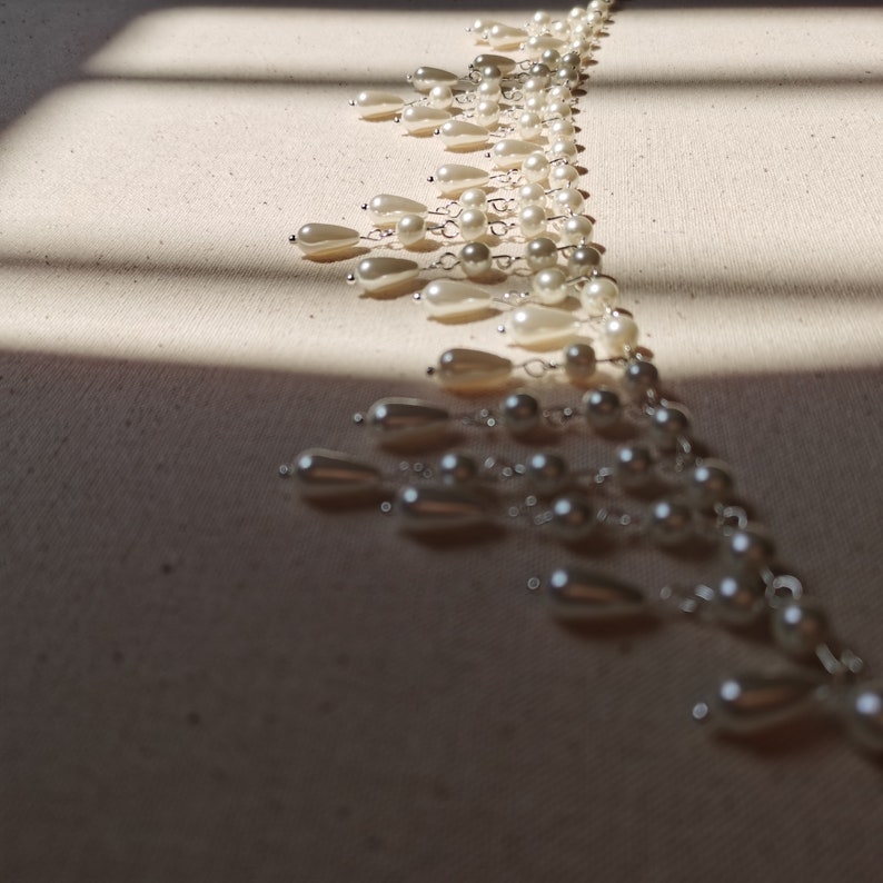 Op de afbeelding: Een lange streng witte parels met zilveren kettingaccenten. De parels zijn in een cascade-patroon gerangschikt, wat een delicate en elegante uitstraling cre&euml;ert.