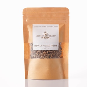 Könnte beinhalten: Ein brauner Papierbeutel mit einem Sichtfenster, das getrocknete Teufels-Kralle-Wurzel zeigt. Der Beutel hat ein weißes Etikett mit dem Text "BOTANICALS - HERBS - POWDERS - RESINS" und ein Logo mit dem Text "MOON MYSTICRAFT". Das Etikett zeigt auch "DEVIL'S CLAW ROOT 30 g | 1 oz."