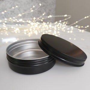 May include: A black metal tin with a silver interior and a black lid. The lid has a raised edge around the top.