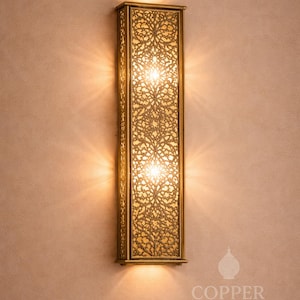 Peut inclure: Applique murale rectangulaire dorée avec un écran à motifs floraux complexes. L'applique a deux lumières et est montée sur un mur brun clair. Le texte "COPPER NOMAD" est visible en bas.
