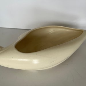 May include: A white ceramic planter shaped like a bird. The planter has a smooth, glossy finish and a slightly curved shape.