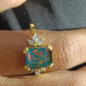 Puede incluir: Un anillo de oro con una piedra preciosa verde, roja y naranja rodeada de pequeños diamantes.