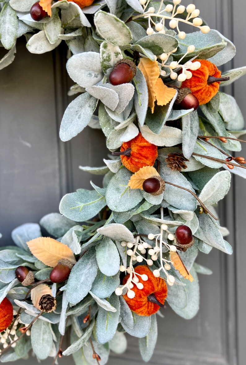 Puede incluir: Una corona de oto&ntilde;o verde, gris y marr&oacute;n con calabazas de terciopelo, bellotas y bayas blancas.