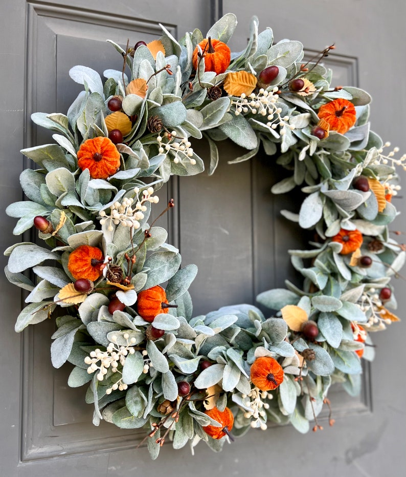 Puede incluir: Una corona verde y blanca con calabazas de terciopelo naranja y detalles marrones. La corona est&aacute; hecha de vegetaci&oacute;n artificial y es perfecta para la decoraci&oacute;n de oto&ntilde;o.