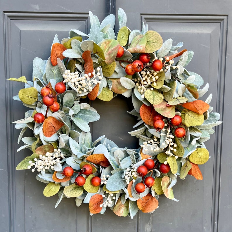 May include: A fall-themed wreath with green, orange, and white leaves and red berries. The wreath is made of artificial materials and is suitable for decorating a door or wall.