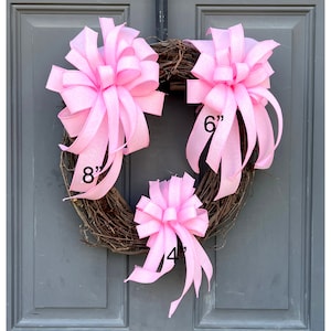 May include: Three pink fabric bows of different sizes, 4 inches, 6 inches, and 8 inches, on a brown twig wreath.
