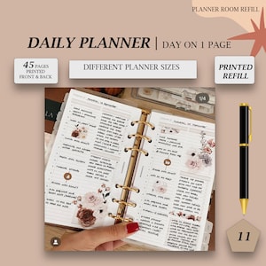 May include: A daily planner with a gold binder and floral stickers. The planner has 45 pages and is printed front and back. The planner is open to a Monday and Tuesday page. The planner is labeled "Daily Planner" and "Day on 1 Page".