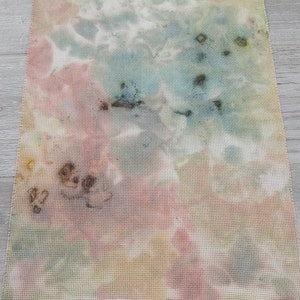 May include: A piece of fabric with a tie-dye pattern in shades of pink, blue, yellow, and brown. The fabric has a grid-like texture.
