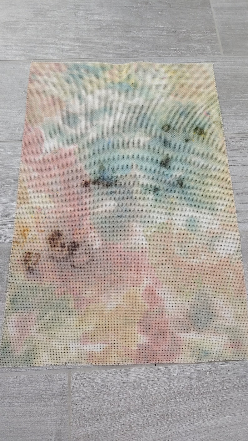 May include: A piece of fabric with a tie-dye pattern in shades of pink, blue, yellow, and brown. The fabric has a grid-like texture.