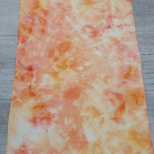 May include: A tie-dye fabric swatch in shades of orange, yellow, and pink. The fabric has a white background with a tie-dye pattern.