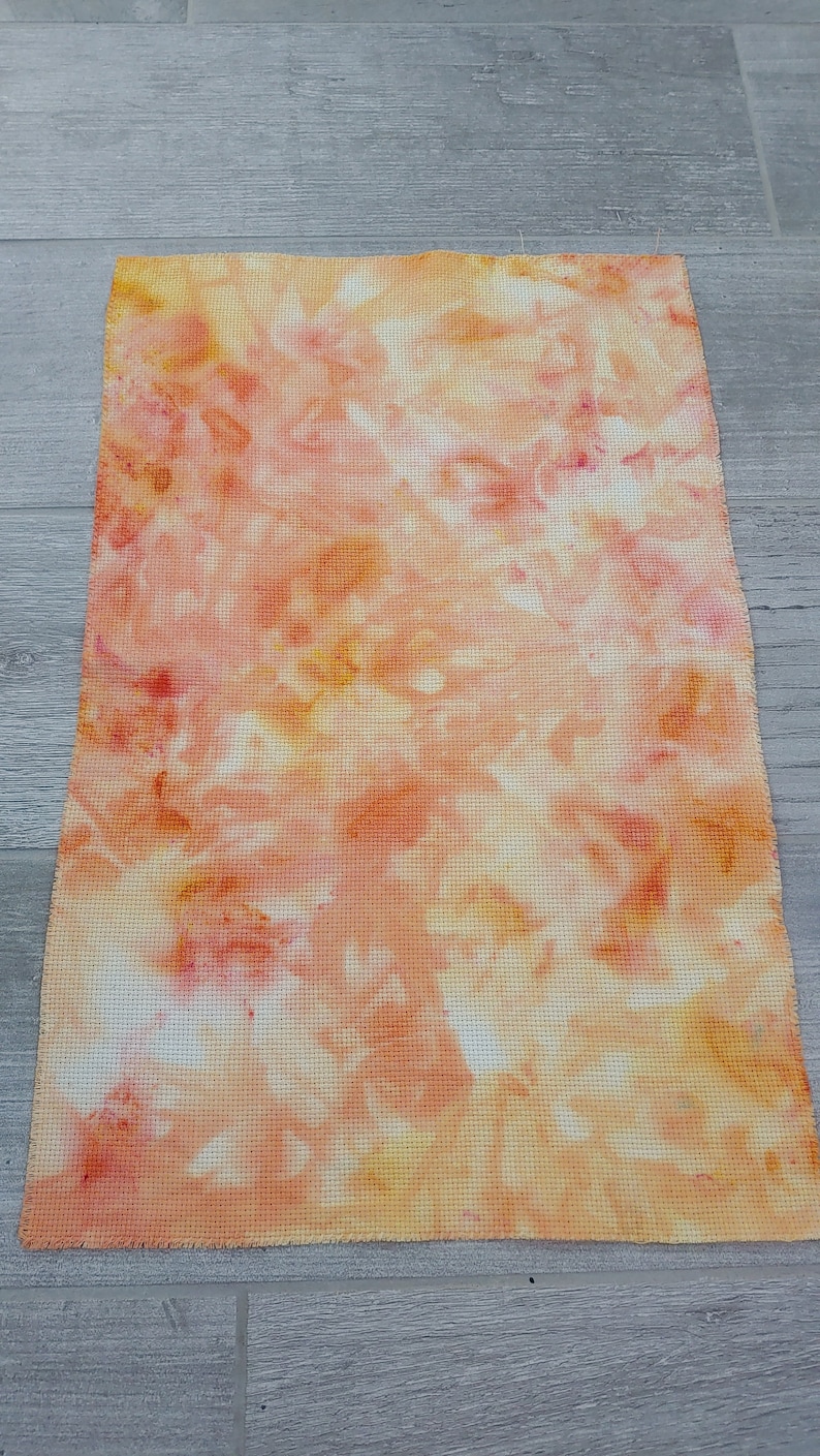 May include: A tie-dye fabric swatch in shades of orange, yellow, and pink. The fabric has a white background with a tie-dye pattern.