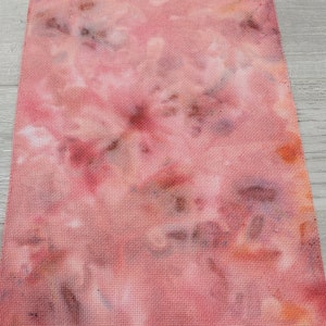 May include: A piece of pink and brown tie-dye fabric with a grid pattern. The fabric is a light pink color with brown and orange spots.