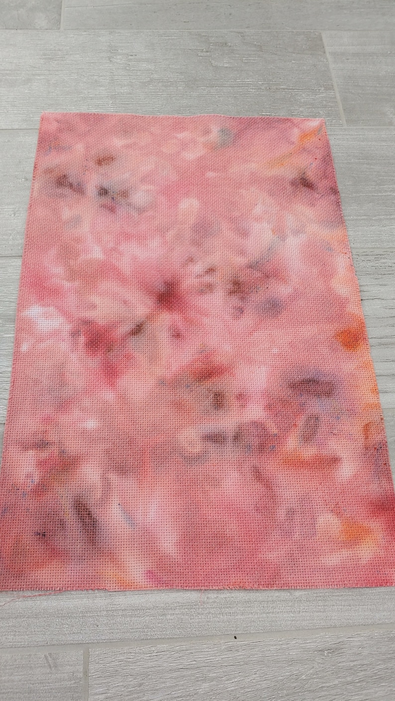 May include: A piece of pink and brown tie-dye fabric with a grid pattern. The fabric is a light pink color with brown and orange spots.