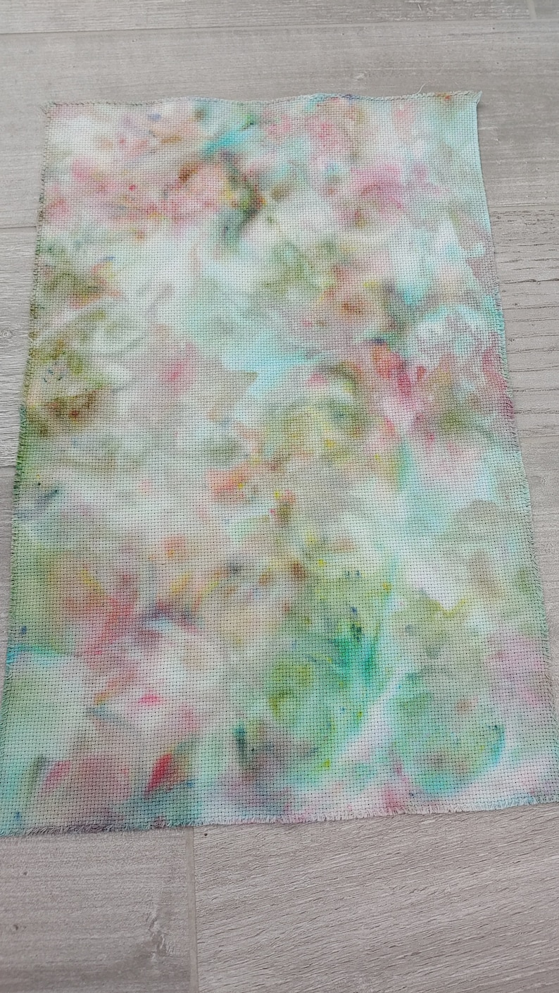 May include: A piece of white fabric with a tie-dye pattern in shades of pink, blue, green, and yellow.