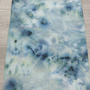 May include: A piece of white fabric with a blue and green tie-dye pattern. The fabric has a subtle grid pattern.