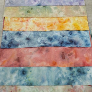 May include: A stack of eight fabric squares in various shades of blue, green, yellow, orange, and pink. The fabric has a subtle texture and a tie-dye pattern.