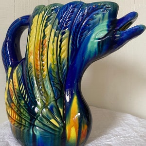 May include: A blue and yellow ceramic pitcher shaped like a bird with a detailed design. The pitcher has a wide mouth and a handle.