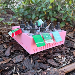 May include: A pink display box containing multiple black and clear wallflower fragrance refills. The box is labelled with the word "wallflowers". Several refills have tags attached, with text such as "Letters to the North Pole".