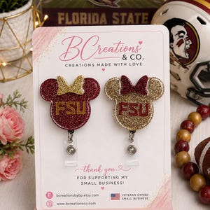 May include: Two glittery mouse-shaped badge reels mounted on a display card. The left reel is maroon with a gold bow and FSU text, while the right is gold with a maroon bow and FSU text. Both feature clear plastic clips and are labeled BCreations & CO.