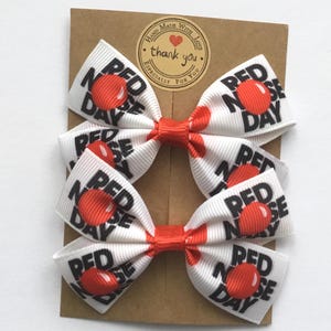Red and white school hair bows featuring large red nose character prints. Set of 2 boutique bows for girls Red Nose Day celebration.