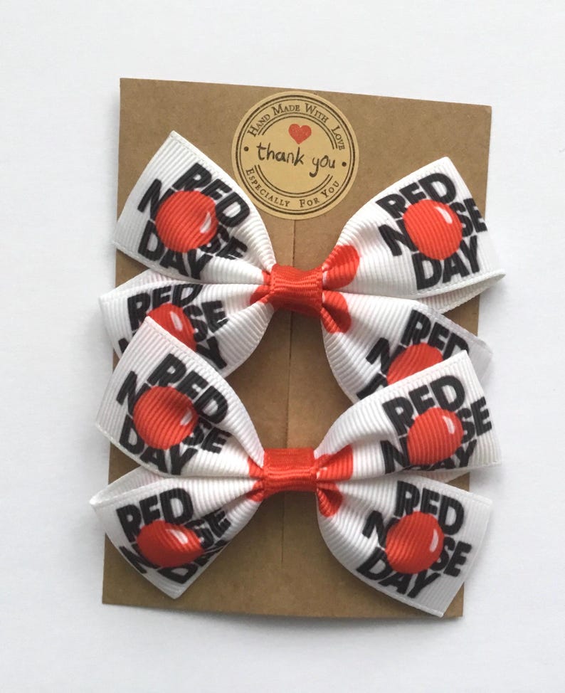 Red and white school hair bows featuring large red nose character prints. Set of 2 boutique bows for girls Red Nose Day celebration.