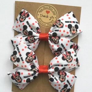 Minnie Mouse themed Red Nose Day hair bows, white ribbon with red polka dots and character print. Cute Disney-inspired charity event accessories.