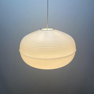 Puede incluir: Una l&aacute;mpara colgante esf&eacute;rica blanca con una pantalla acanalada similar al papel. La luz cuelga de un cable delgado de color plateado. La l&aacute;mpara est&aacute; iluminada, proyectando un brillo suave.
