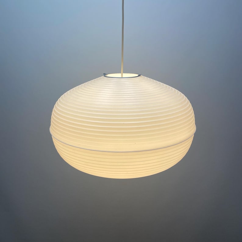 Puede incluir: Una l&aacute;mpara colgante esf&eacute;rica blanca con una pantalla acanalada similar al papel. La luz cuelga de un cable delgado de color plateado. La l&aacute;mpara est&aacute; iluminada, proyectando un brillo suave.