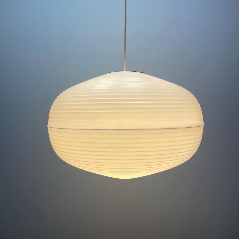 Puede incluir: L&aacute;mpara colgante esf&eacute;rica blanca con superficie texturizada y acanalada. La l&aacute;mpara cuelga de un fino cable blanco sobre un fondo azul. La l&aacute;mpara est&aacute; iluminada, emitiendo un brillo suave. Di&aacute;metro aproximado de 30 cm.