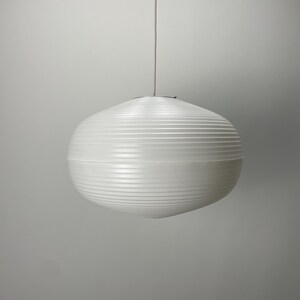 Puede incluir: Una l&aacute;mpara colgante esf&eacute;rica blanca con detalles acanalados horizontales. La luz cuelga de un fino cable blanquecino sobre un fondo gris neutro. La l&aacute;mpara tiene un dise&ntilde;o moderno y minimalista.