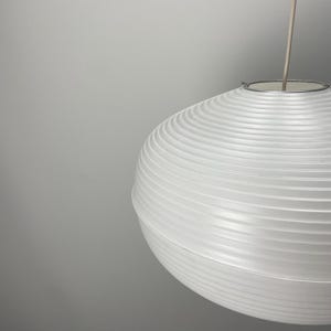 Puede incluir: Una l&aacute;mpara colgante esf&eacute;rica blanca con una pantalla acanalada similar al papel. La luz cuelga de un fino anillo de metal plateado y un cable delgado. El dise&ntilde;o es minimalista y moderno, adecuado para la iluminaci&oacute;n interior.