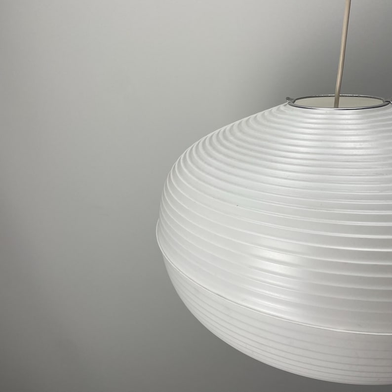 Puede incluir: Una l&aacute;mpara colgante esf&eacute;rica blanca con una pantalla acanalada similar al papel. La luz cuelga de un fino anillo de metal plateado y un cable delgado. El dise&ntilde;o es minimalista y moderno, adecuado para la iluminaci&oacute;n interior.