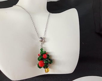 May include: A silver chain necklace with a Christmas tree pendant. The pendant is made of green and red beads, with a small gold-colored base. The necklace is displayed on a white mannequin.
