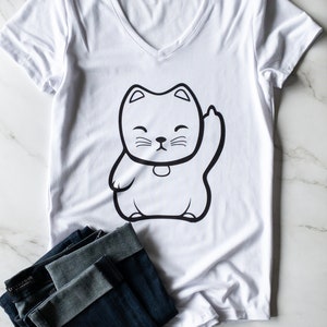 May include: White v-neck t-shirt with a black and white illustration of a cartoon cat giving a thumbs up. The cat is wearing a collar with a bell.