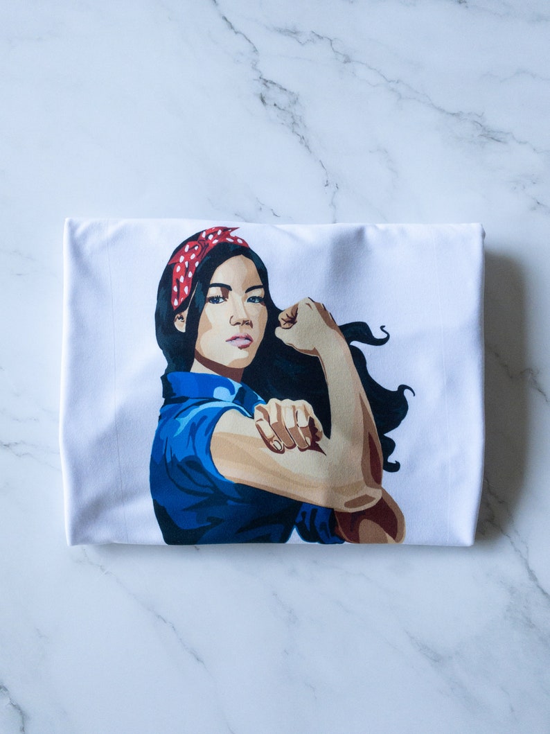 May include: White t-shirt with a graphic of a woman with a red and white polka dot headband, blue shirt, and a flexed arm.