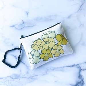 May include: A rectangular off-white pouch with a black zipper and wrist strap. The pouch features a floral design in shades of yellow and green. The background is a marble pattern.
