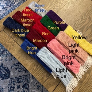 May include: A collection of colorful knitted headbands with fringe, in shades of silver tinsel, red tinsel, maroon tinsel, dark blue tinsel, bright blue, maroon, red, green, purple, yellow, light pink, bright pink, and light blue.