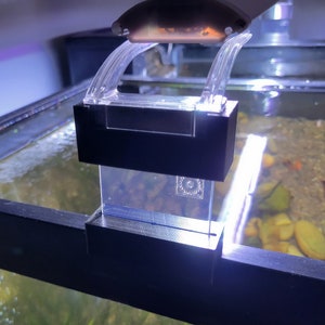 May include: A black and clear plastic aquarium light fixture with a white LED light. The light is mounted on the top of the aquarium and has a clear plastic cover.