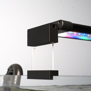 May include: Black aquarium light fixture with a clear acrylic mounting bracket. The light has a multi-colored LED strip.