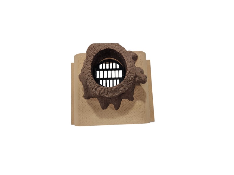 May include: A brown ceramic vent cover with a round, open, metal grate. The vent cover is designed to look like a tree trunk with a hole in it.