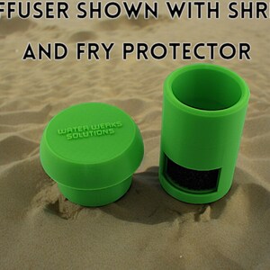 Peut inclure: Deux diffuseurs d'aquarium en plastique vert, l'un avec un dessus rond et l'autre de forme cylindrique. Le diffuseur rond porte l'inscription "Water Werks Solutions". Le diffuseur cylindrique contient une &eacute;ponge noire. Les deux diffuseurs sont pos&eacute;s sur une surface sablonneuse.