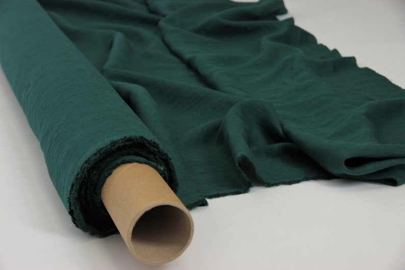 May include: A roll of dark green fabric, likely linen or cotton, is shown on a white surface. The fabric is folded and rolled up, with the end of the roll visible.