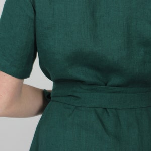 May include: A dark green linen dress with a self-tie belt. The dress has a simple, classic design and is perfect for a variety of occasions.