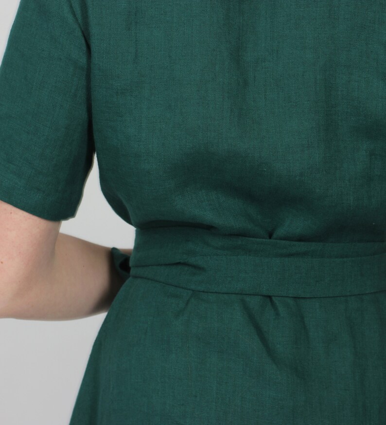 May include: A dark green linen dress with a self-tie belt. The dress has a simple, classic design and is perfect for a variety of occasions.